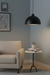 Beige armchair in a room with a black pendant light, small table, and framed pictures on the wall.