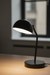 Black table lamp on a wooden surface with a blurred window in the background