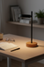 Desk lamp on a wooden desk with books, glasses, and a pen in a home office setting.