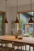 Dining area with wooden table and chairs in a room with large windows showing a view of a house and trees.