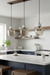 Modern kitchen with pendant lights, white countertops, and wooden stools.