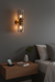 Modern wall sconce on a gray wall above a wooden nightstand with a smartphone and plant.