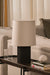 Black and Beige origami lamp on a table with a sofa and striped curtains in the background