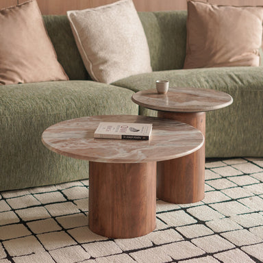 Two wooden coffee nesting tables in front of a green sofa with beige cushions on a tiled floor.