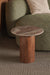 Wood and marble side table in front of a green sofa with a neutral pillow.