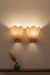 Two wall-mounted lamps with checkered shades on a plain wall, with a green vase and dried plants on a shelf below.