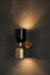 Wall-mounted light fixture with black and gold design on a dark wall.