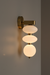 Wall-mounted light fixture with three round glass shades on a plain wall.