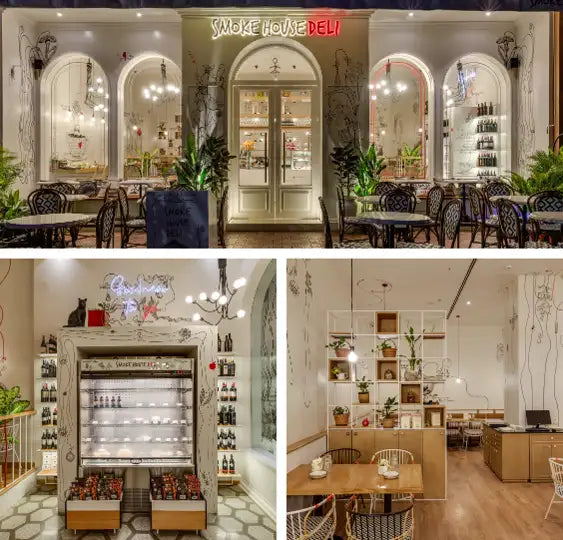 The ’smoke house deli’ storefront features arched windows, a white double door with glass panels and gold hardware, flanked by potted plants under warm lighting.