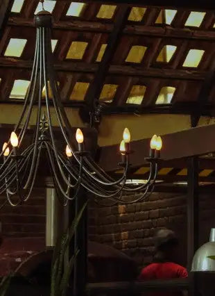 Black wrought iron chandelier with multiple arms and lit bulbs.