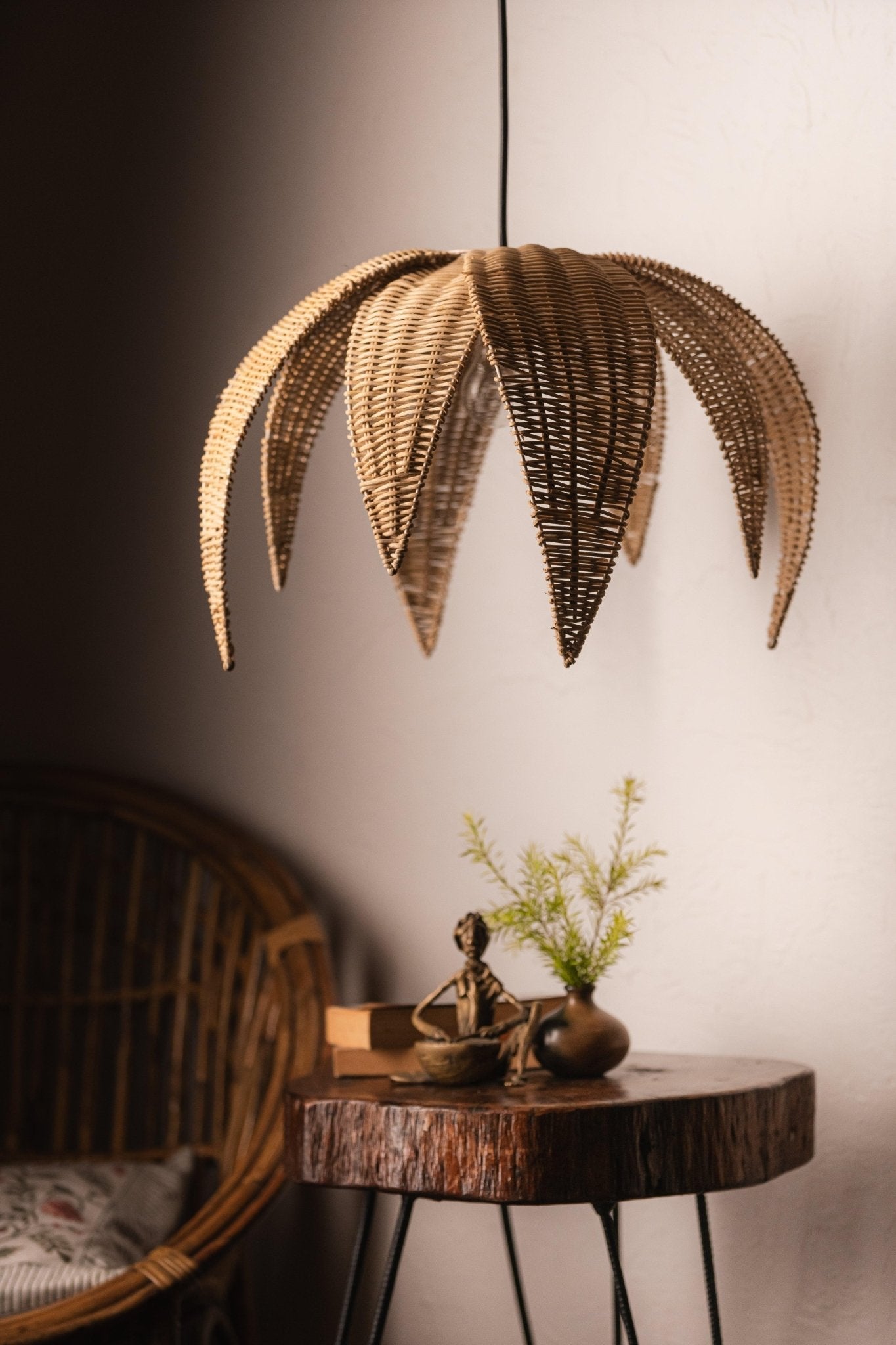 Wicker palm leaf pendant light hanging above a wooden table with decor items.