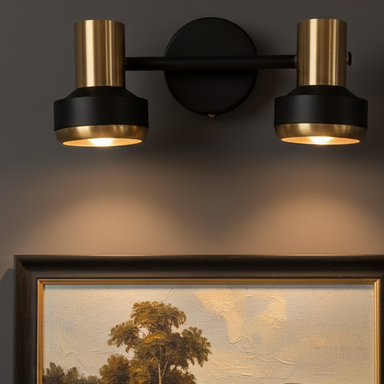 Wall-mounted light fixture with two gold bulbs on a dark wall above a framed landscape painting.